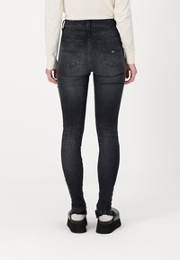 Vaqueros ajustados de color gris oscuro con diseño de cinco bolsillos y pasadores para cinturón. Hechos de denim, presentan un ligero desgaste y una textura suave.
