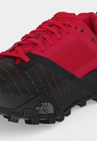 Κόκκινο και μαύρο παπούτσι North Face για μονοπάτι με ανθεκτική σόλα, κόκκινα κορδόνια και ετικέτα Gore-Tex στο πλάι.