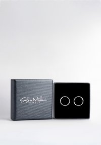 Silver hoop earrings displayed in a black velvet box with a textured, dark gray exterior and the brand name printed in white.