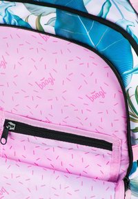 Interiér batohu s růžovým podšívkou a rozptýleným vzorem posypky. Černý zip s táhlem a květinový design na vnějším materiálu.