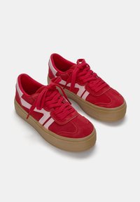 Baskets en daim rouge avec des accents roses, bout rond, semelle en caoutchouc épaisse et lacets plats. Présentent des panneaux texturés et des rayures diagonales.