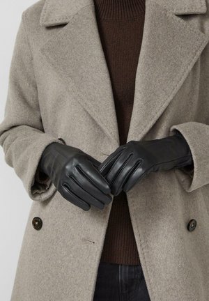 Czarne skórzane rękawiczki o gładkiej fakturze z nacięciami z tyłu, noszone razem z beżowym płaszczem i pod nim brązowym dzianym swetrem.