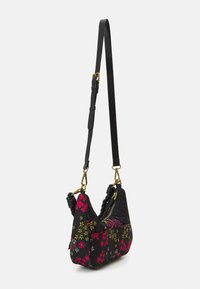 Malá černá crossbody taška s červeným a žlutým květinovým potiskem, zlatým zipem, pletenými detaily na rukojeti a nastavitelným ramenním popruhem se zlatou sponou.