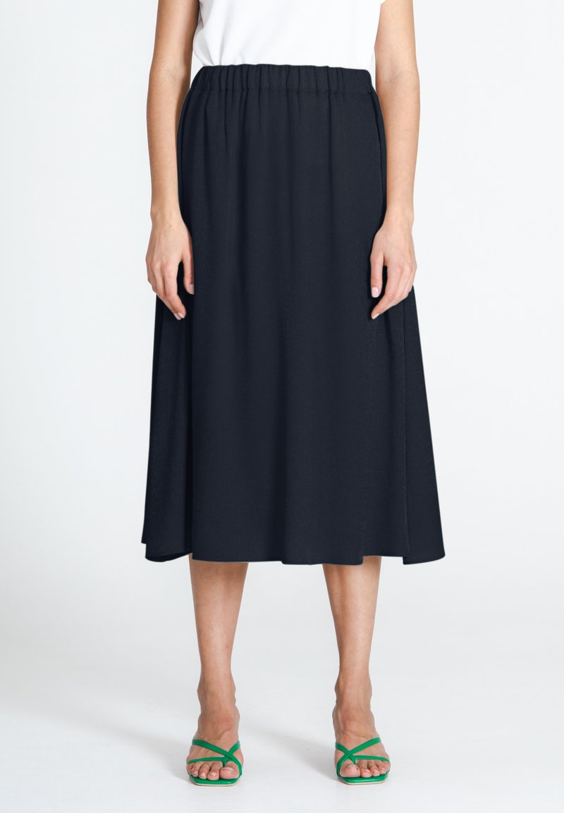 Falda midi negra con cintura elástica, que presenta una silueta fluida y una textura suave. Combinada con sandalias verdes de tiras.
