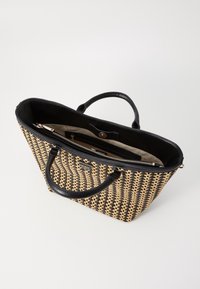 Sac tote tissé avec un motif noir et naturel, présentant des poignées et des bordures en cuir noir, une fermeture éclair et un intérieur beige avec des poches.
