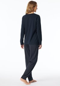 Marineblauw langemouwen top gecombineerd met gestreepte pyjamabroek. Zachte stof, relaxte pasvorm en taps toelopende manchetten; minimalistisch ontwerp met geometrische accenten.