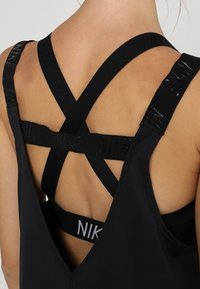 Vista trasera de una persona que lleva ropa deportiva negra con correas elásticas de marca Nike que se intersectan en la parte superior de la espalda desnuda.