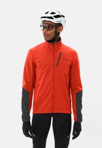 Giacca da ciclismo rossa con cerniera, dettagli grigi, tessuto elastico, colletto alto e tasca con cerniera inclinata sul petto. Guanti neri e pantaloni corti.