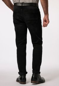 Jeans in denim nero con vestibilità slim, orlo arrotolato e due tasche posteriori. Indossati con scarpe in pelle nere, che mostrano una silhouette dritta.
