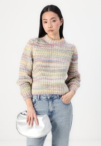 Pull en laine multicolore avec une texture côtelée et un col montant, associé à un jean en denim bleu clair et à un sac à main métallisé argent.