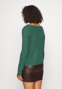 Grüner Strickpullover mit weitem Ausschnitt, strukturierter Stoff und langen Ärmeln, kombiniert mit einem braunen Leder-Minirock.