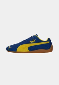 Blauwe suède sportschoenen met gele accenten, voorzien van een gestructureerd oppervlak en rubberen zool. Logo op de zijkant gedrukt. Laag gesneden ontwerp.