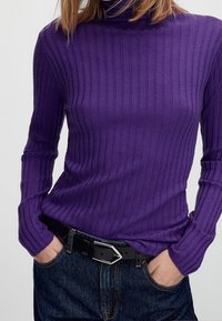 Paarse geribbelde coltrui met lange mouwen, gecombineerd met een zwarte riem en hooggetailleerde spijkerbroek met een klassieke pasvorm.