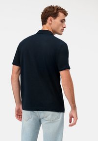 Marineblaues Poloshirt aus Baumwolle mit klassischem Kragen und kurzen Ärmeln. Getragen mit hellblauen Jeans, die einen lässigen Look unterstreichen.