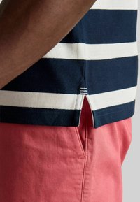 Zili un balti svītrots polo krekls ar sānu šķēlumu, apvienots ar rozā biksēm. Iespējo fakturēts audums un kontrastējoša apkakle.