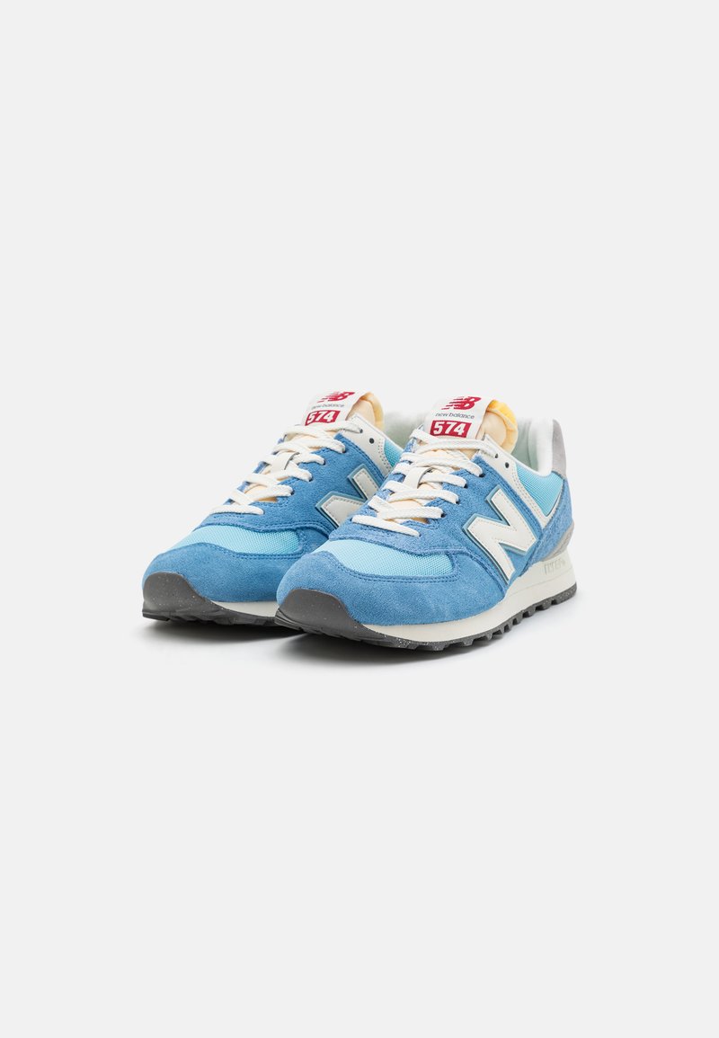 Helle blaue Sneaker aus Wildleder und Mesh-Material, mit weißen Akzenten, Schnürsenkeln, einer grauen Sohle und rotem Branding auf der Zunge. Modell 574.