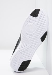 Black sneaker with a textured gray upper and a white rubber sole. Underfoot features a patterned grip with a circular center design.