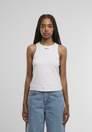 White sleeveless tank top with a round neckline and embroidered logo at the chest. Worn with light blue high-waisted denim jeans.