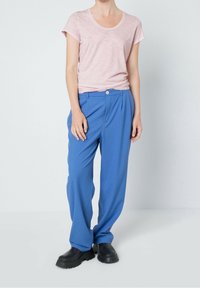 Różowa koszulka z krótkim rękawem z okrągłym dekoltem, zestawiona z niebieskimi spodniami o szerokim kroju z przodu i z zapięciem na guzik. Czarne, masywne buty.