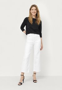 Haut noir à manches longues associé à un jean blanc taille haute et large, ainsi qu'à des talons noirs à lanières ; tissu lisse et coupe ajustée.