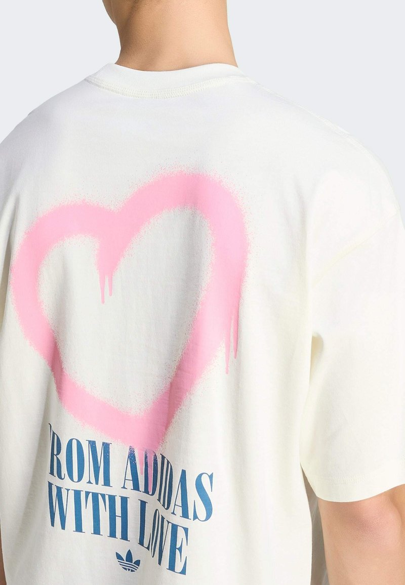 Person trägt ein weißes Hemd mit einem großen, pinken, gesprayten Herz und blauer Schrift "FROM ADIDAS WITH LOVE" auf dem Rücken.