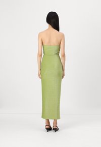 Vestido midi verde, sem mangas, em um tecido cintilante, ajustado na cintura, com uma textura suave e silhueta reta, usado com sapatos de salto pretos.