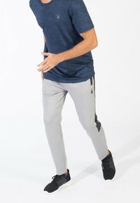 Námořnická modrá maskáčová tričko s logem; světle šedé jogger kalhoty s černými bočními akcenty; nošeno s černými teniskami.