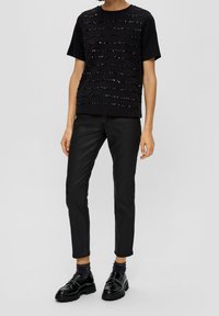 Svart kortärmad T-shirt med texturerade horisontella ränder av paljetter, i kombination med svarta slim-fit byxor och glänsande svarta loafers.