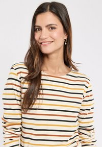 Gestreepte lange mouw top met zwarte, oranje en gele strepen op een roomkleurige achtergrond, ronde halslijn en zachte stof textuur.