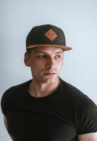 Black cap with a speckled texture, leather patch featuring a diamond shape, and a flat brim. Worn with a plain black T-shirt.