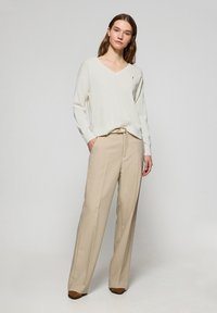 Pull en V beige avec des manches longues associé à un pantalon large beige. Ceinture marron remarquable en accent. Textures douces avec une coupe décontractée.