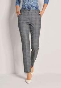 Grijze geruite broek met een getailleerde pasvorm, voorzien van zakken, een knoopsluiting en een soepel materiaal. Draagt met puntige witte hakken.