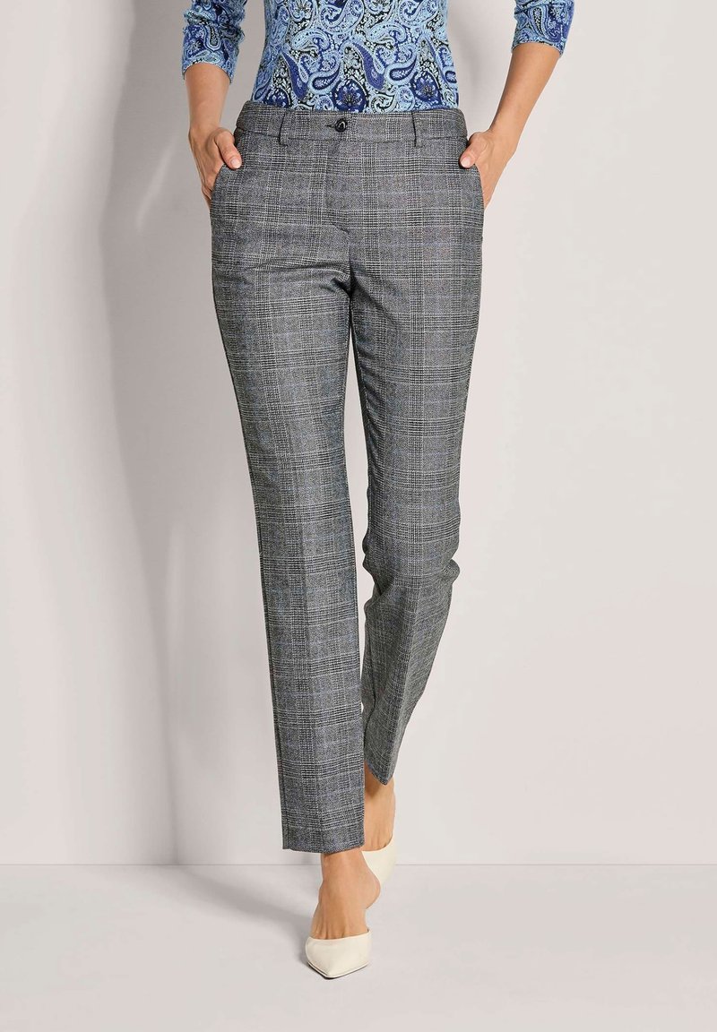 Grijze geruite broek met een getailleerde pasvorm, voorzien van zakken, een knoopsluiting en een soepel materiaal. Draagt met puntige witte hakken.