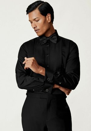 Czarna koszula smokingowa z plisowanym przodem, z detalami w postaci guzików i pasującą muszką. Gładki materiał i dopasowany krój z kontrastowymi mankietami.