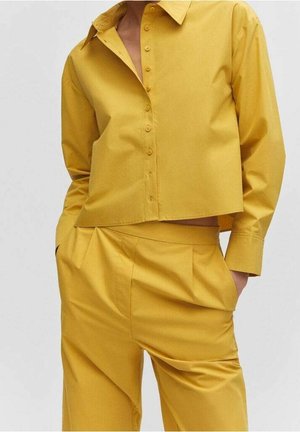 Żółta krótka koszula na guziki wykonana z gładkiej tkaniny, z klasycznym kołnierzem i długimi rękawami, zestawiona z pasującymi, wysokim stanem spodniami.