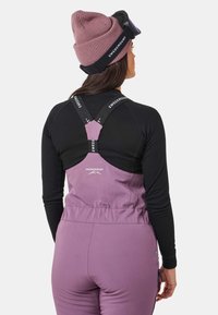 Paarse skibroek met zwarte lange mouwen, voorzien van verstelbare bandjes met logo en een hoge rug voor extra bedekking. Textuurover oppervlak en zichtbare zakken.