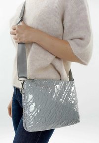 Bolso de mano gris acolchado con un acabado brillante, que presenta una correa desmontable, forma rectangular y un patrón de costura diagonal.
