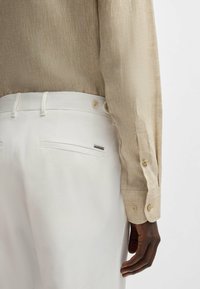 Long-sleeve beige linen shirt with a textured finish, paired with white tailored pants featuring back pockets and a metallic accent.