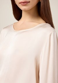 Helles Beige, weiter Ausschnittoberteil aus weichem, glattem Stoff mit lockeren Ärmeln. Dezenter Fall für mehr Komfort, mit minimalistischem Design.