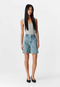 Shorts di denim azzurri con vita alta e gambe larghe, abbinati a una canotta grigia senza maniche. Un paio di scarpe nere a punta completa il look.