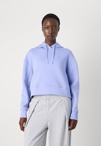 Sweat à capuche court violet clair avec cordons, arborant un petit logo et une coupe décontractée, associé à un pantalon de jogging plissé gris clair.