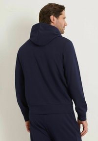 Sudadera azul marino con capucha, fabricada en un tejido suave. Presenta un corte relajado y puños de canalé, mostrada desde la parte posterior.