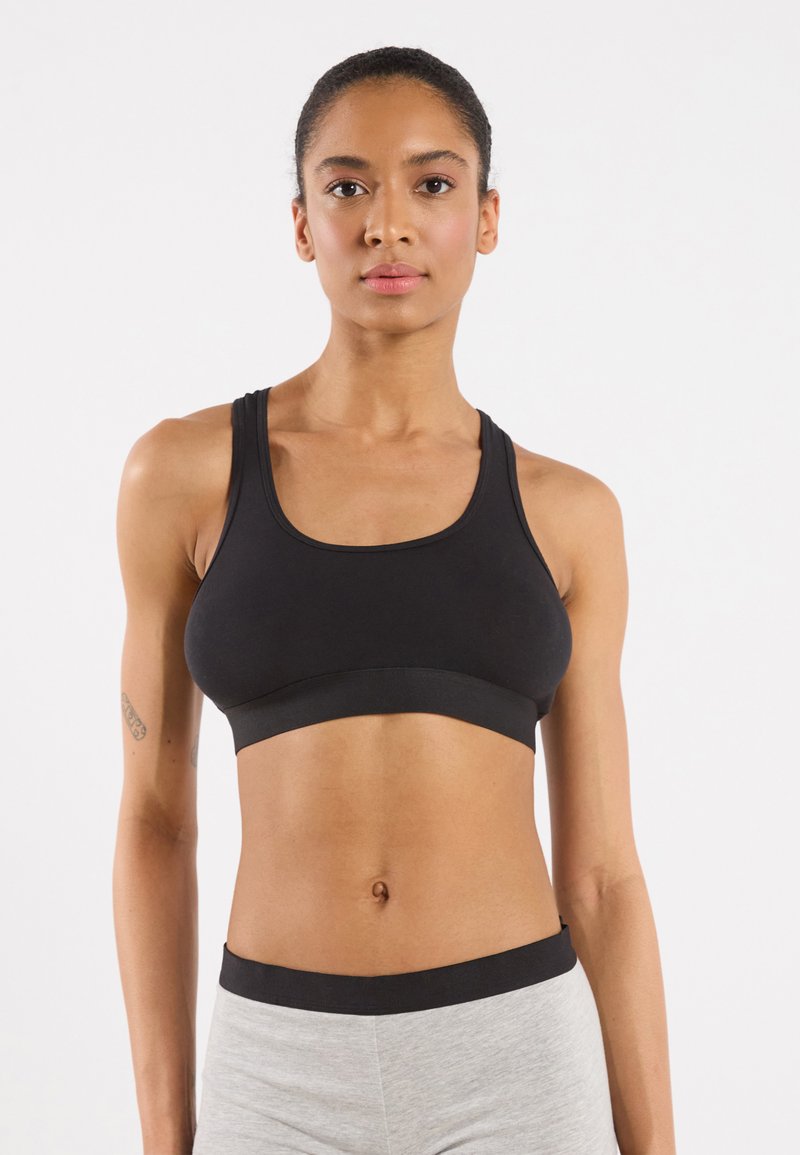 Soutien-gorge de sport noir au design simple, avec des bretelles larges et une bande élastique sous la poitrine. Tissu lisse et coupe ajustée.