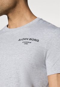 Grey short-sleeve t-shirt made of soft fabric, featuring a black printed logo and text on the upper left side. Classic crew neck design.