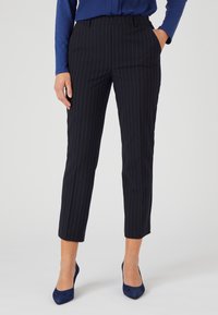 Marineblauwe pinstriped broek met een op maat gemaakte pasvorm, voorzien van een gladde textuur, taps toelopende benen en een middelhoog tailleband, gecombineerd met marineblauwe hakken.