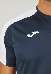 Tumesinine sportlik t-särk valgete õlavarre aktsentidega. Valmistatud kergest kangast, millel on sile tekstuur. Logo on rinnal.