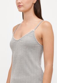 Camisole grise à côtes avec bretelles ajustables, bordure en dentelle festonnée et petits nœuds en accent, fabriquée dans un tissu doux et texturé.