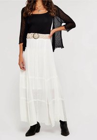 Czarny koronkowy kardigan na czarnym topie, połączony z długą białą spódnicą. Stylizacja uzupełniona jest plecionym beżowym paskiem z okrągłą metalową klamrą.