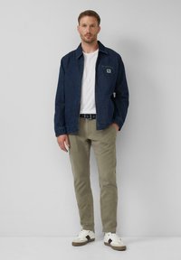 Jeansjack met een voorzak, witte T-shirt, kaki broek en witte sneakers. Het jack heeft een klassieke kraag en een iets losse pasvorm.