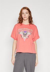 Coral oversized t-shirt made of soft fabric featuring a graphic design of an eagle with the text "Independent Souls." Short sleeves.